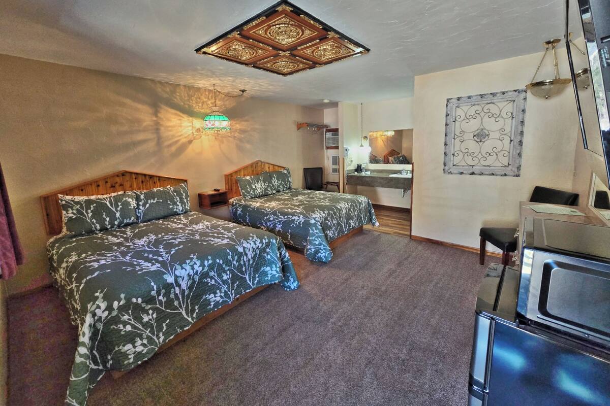 A hotel room with two beds, a desk, a chair, a mirror, and a ceiling light fixture.