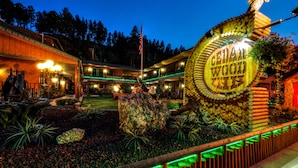 A hotel entrance with a large wooden sign, a flag, and a well-maintained garden area. - Cedar Wood Inn (Deadwood)