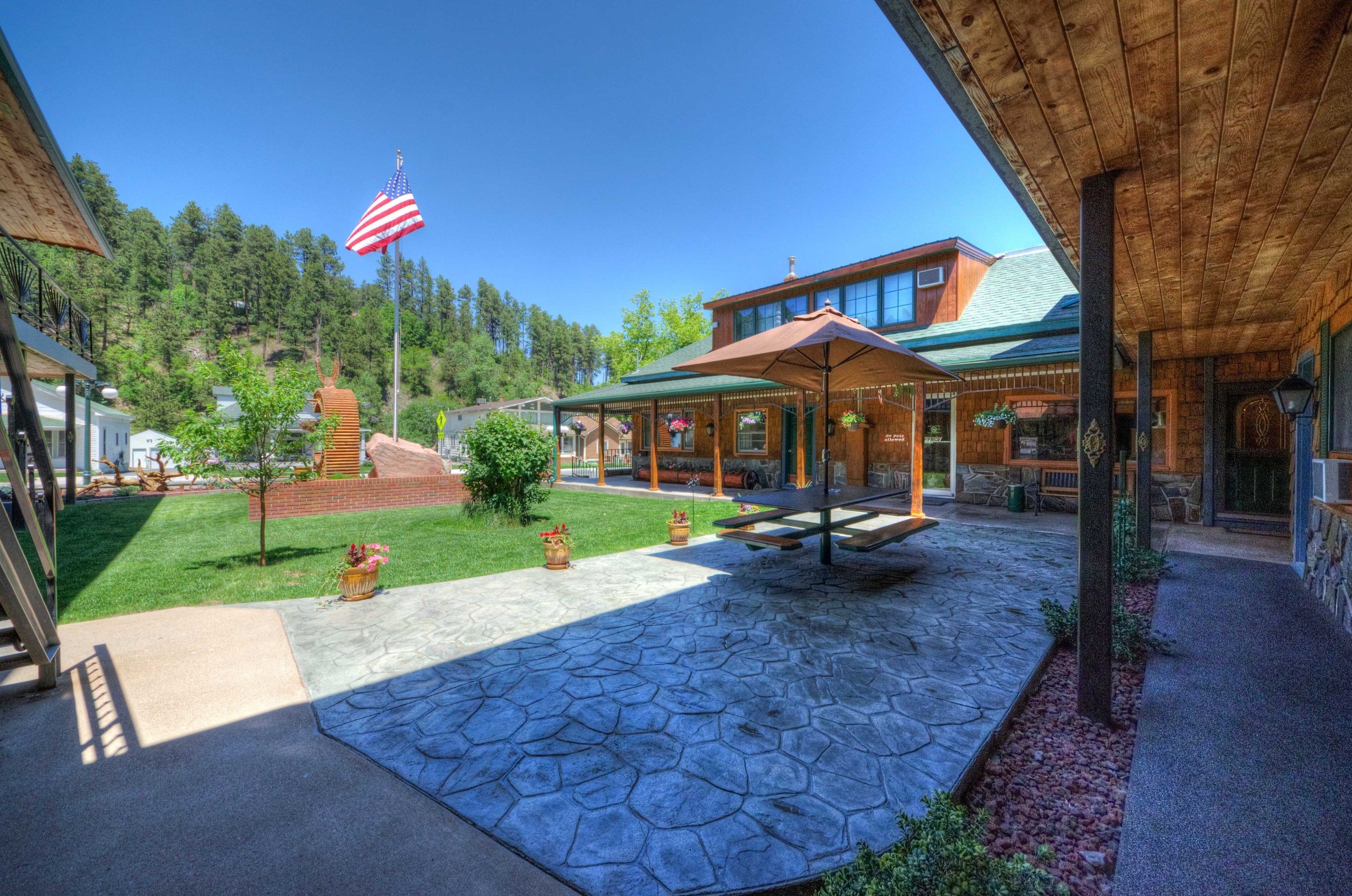 A covered outdoor area with a stone floor, a wooden pergola, and a flagpole with an American flag.