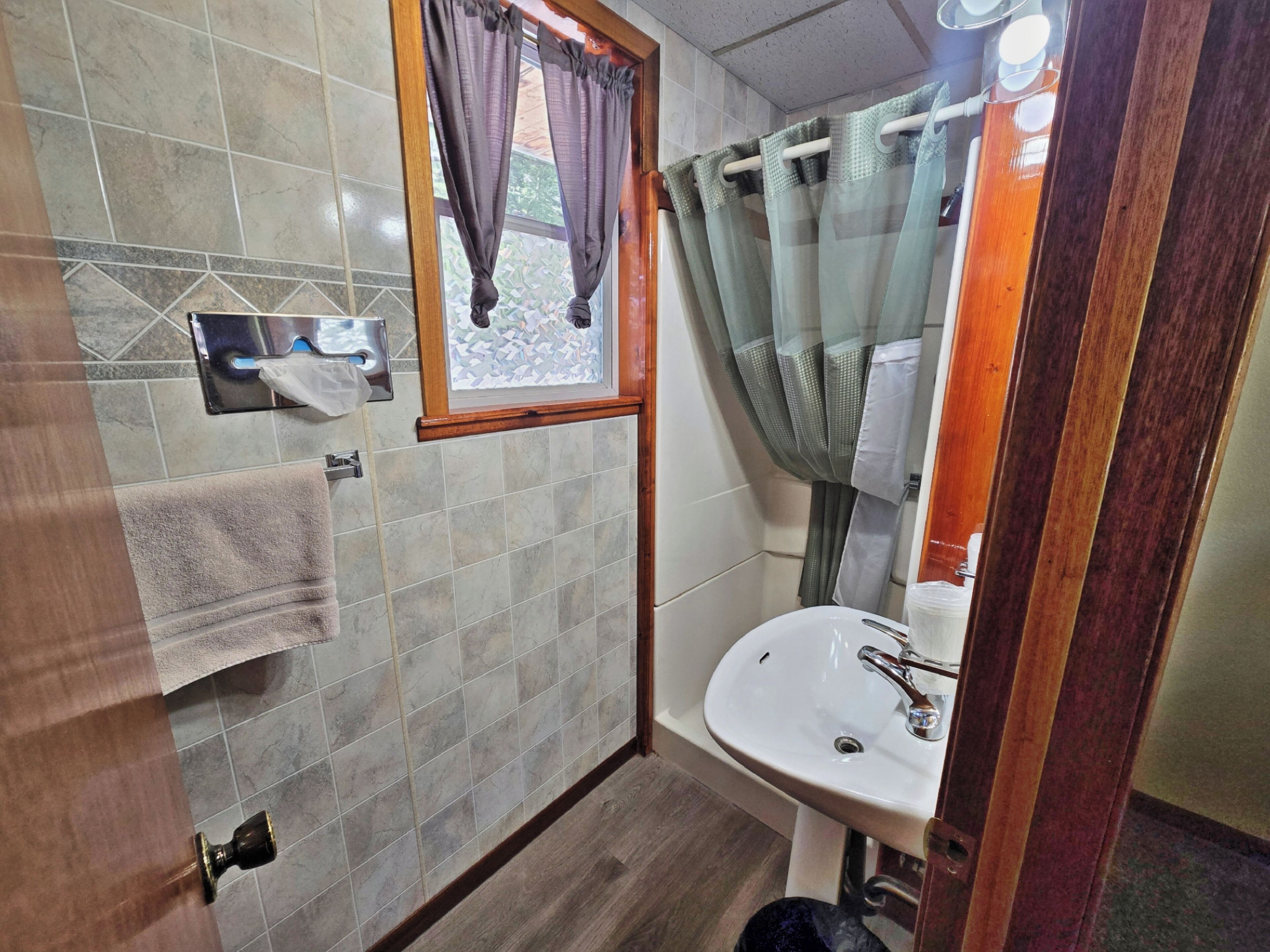 A bathroom with a tiled floor, a sink, a mirror, and a window with curtains.