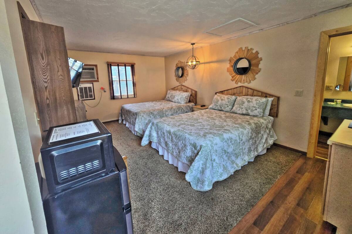A bedroom with two beds, a wooden wardrobe, a desk with a computer, and a bathroom visible through an open door.