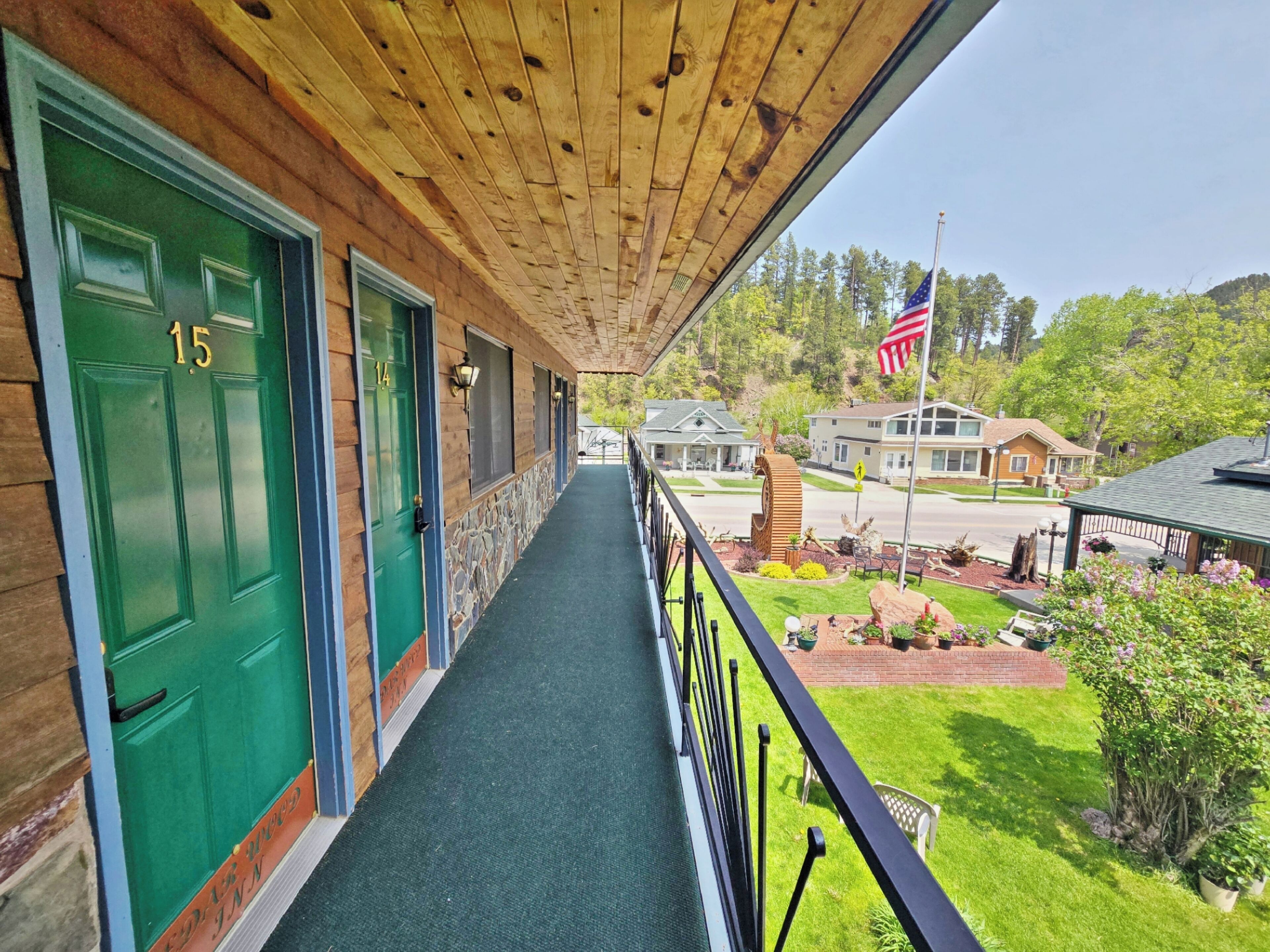 A wooden porch with green doors numbered 15 and 14, leading to a covered walkway.