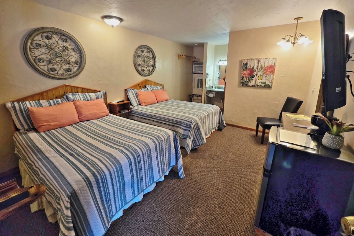 A hotel room with two beds, a desk, a chair, a TV, and decorative wall art.