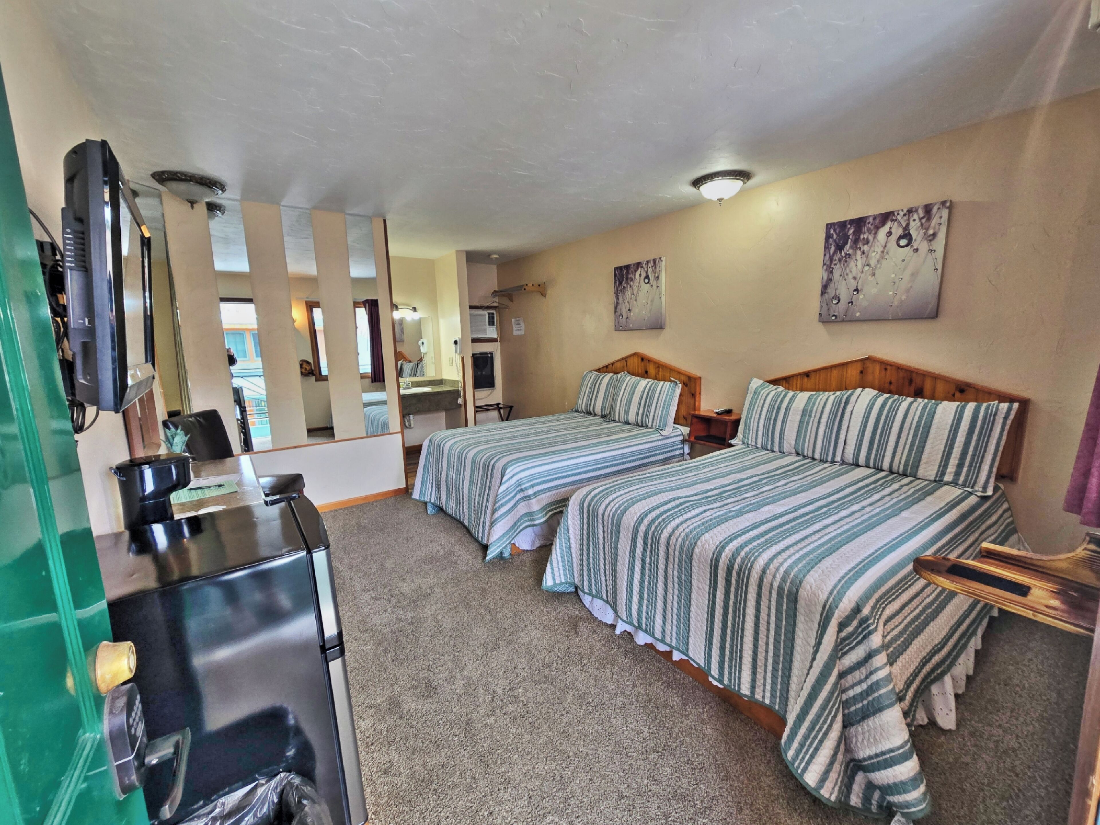 A hotel room with two beds, a desk, a television, and a mirror.