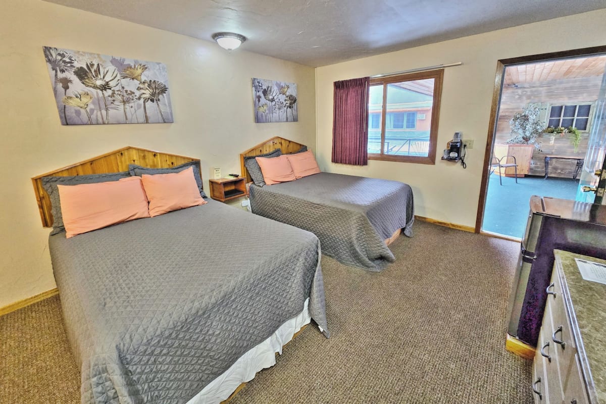 A room with two beds, a wooden headboard, a small nightstand, and a window with curtains.