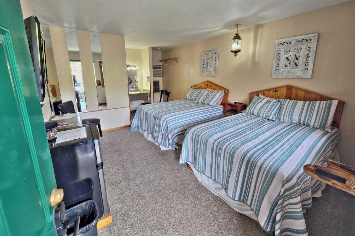 A room with two beds, a desk, a mirror, and a door.