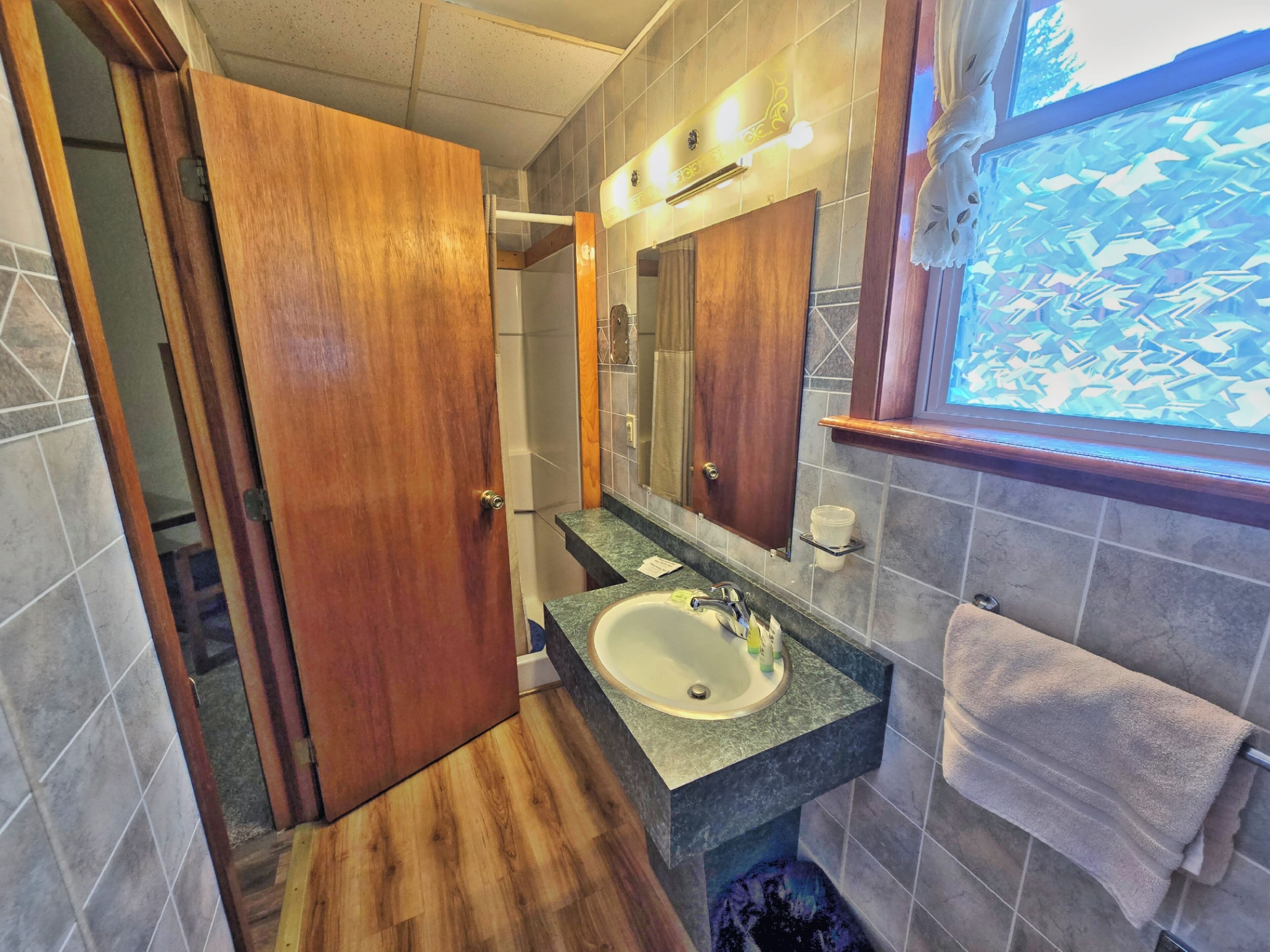 A bathroom with a wooden door, a sink with a mirror above it, and a towel hanging on the wall.