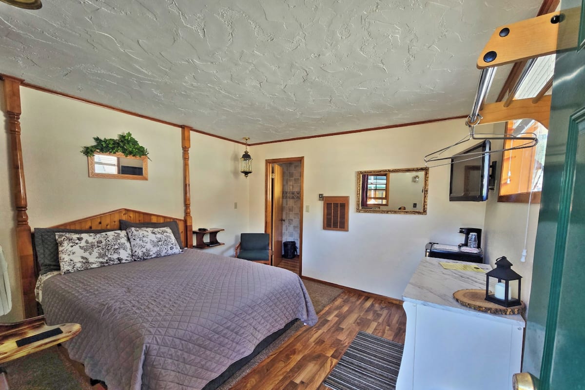A bedroom with a wooden bed, a chair, a desk, a mirror, and a hanging light fixture.