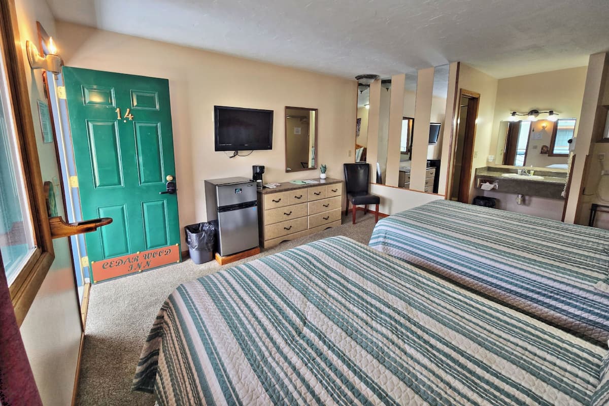 A hotel room with two beds, a dresser, a television, a mirror, and a door with a number.
