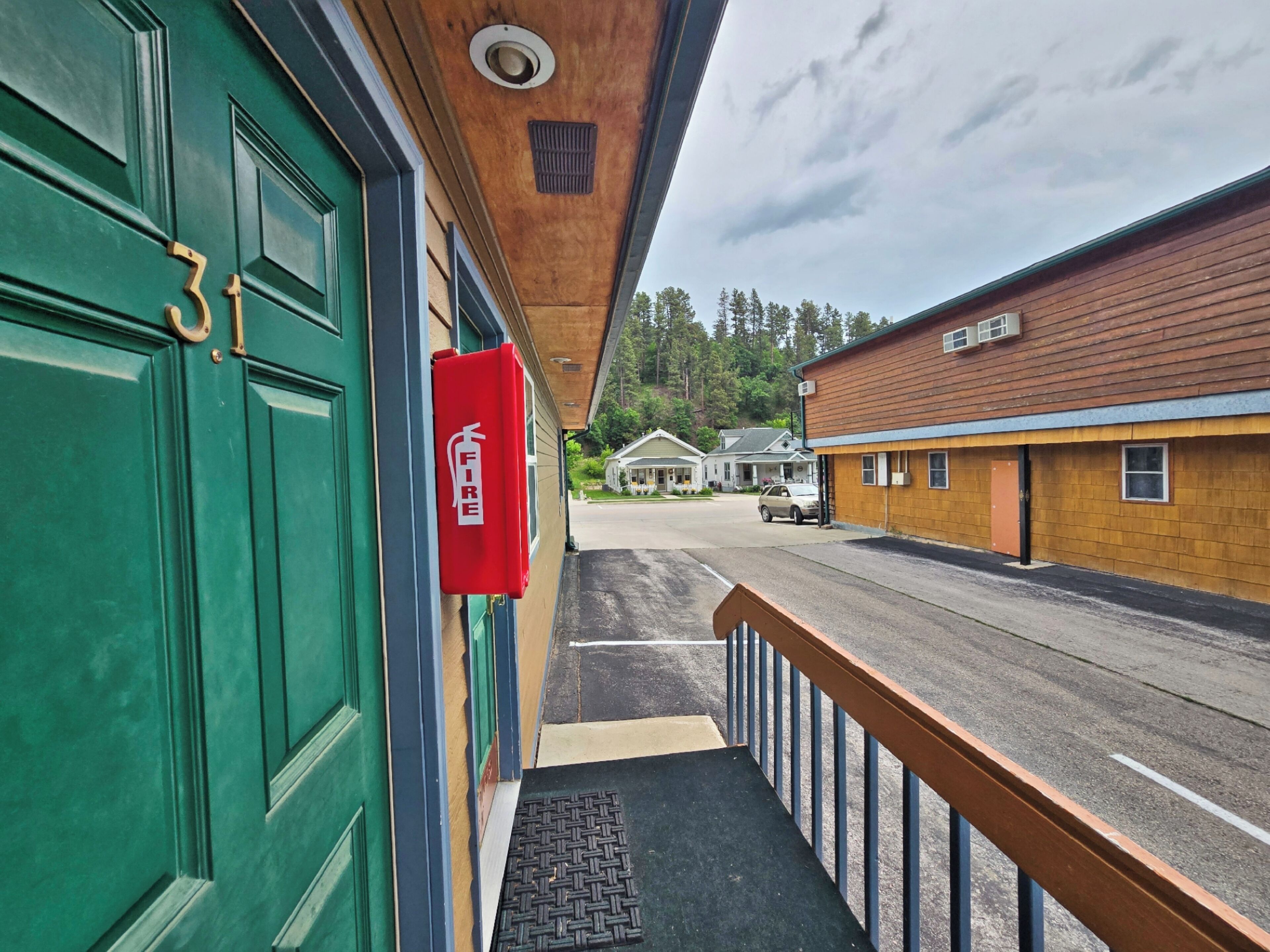 A building with a green door, a fire extinguisher mounted on the wall, and a wooden exterior.