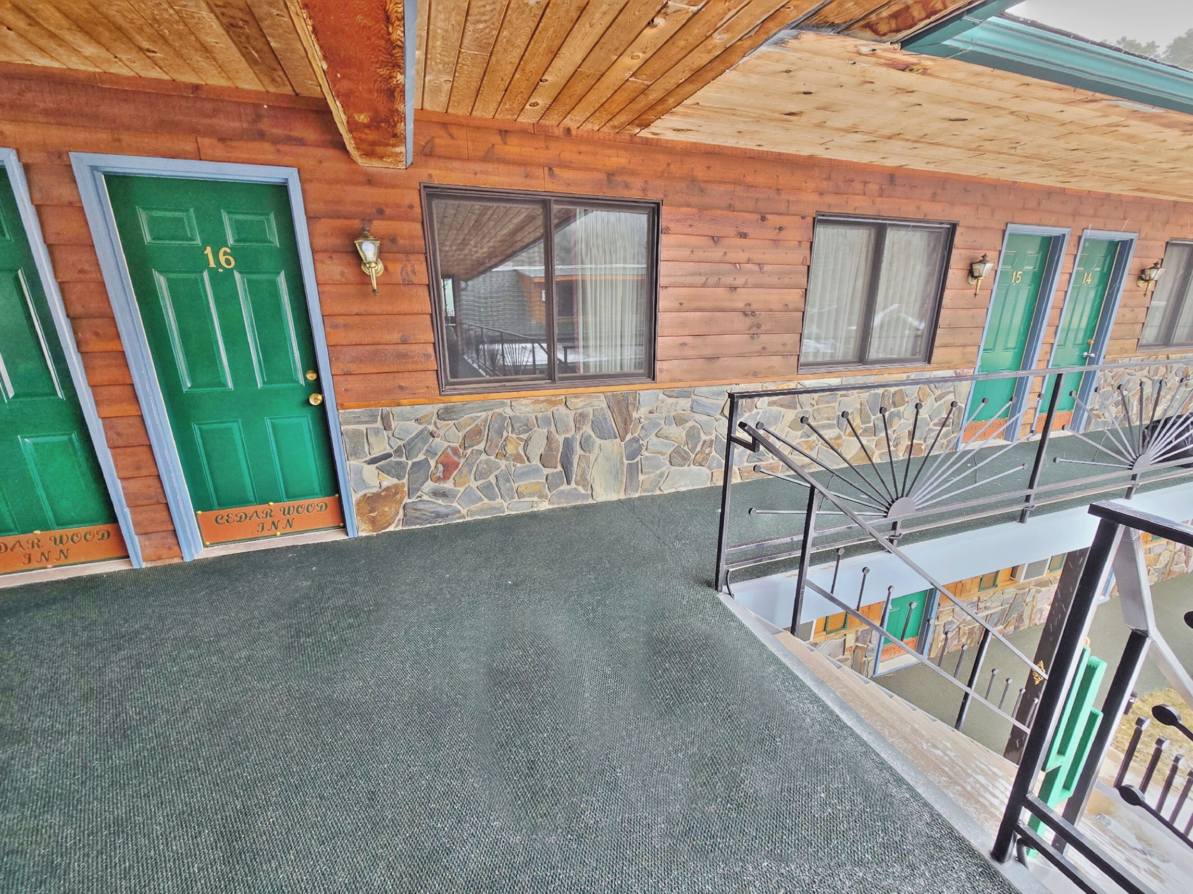 A hotel with a stone facade, green doors, and a metal staircase.