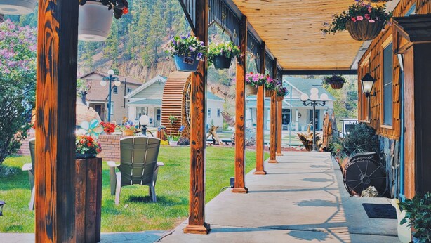 A covered outdoor area with wooden pillars, hanging flower baskets, and a pathway leading to a building labeled "OFFICE". - Cedar Wood Inn (Deadwood)