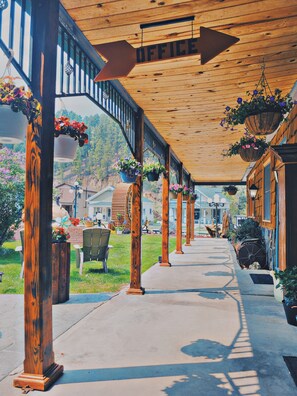 A covered outdoor area with wooden pillars, hanging flower baskets, and a pathway leading to a building labeled "OFFICE". - Cedar Wood Inn (Deadwood)