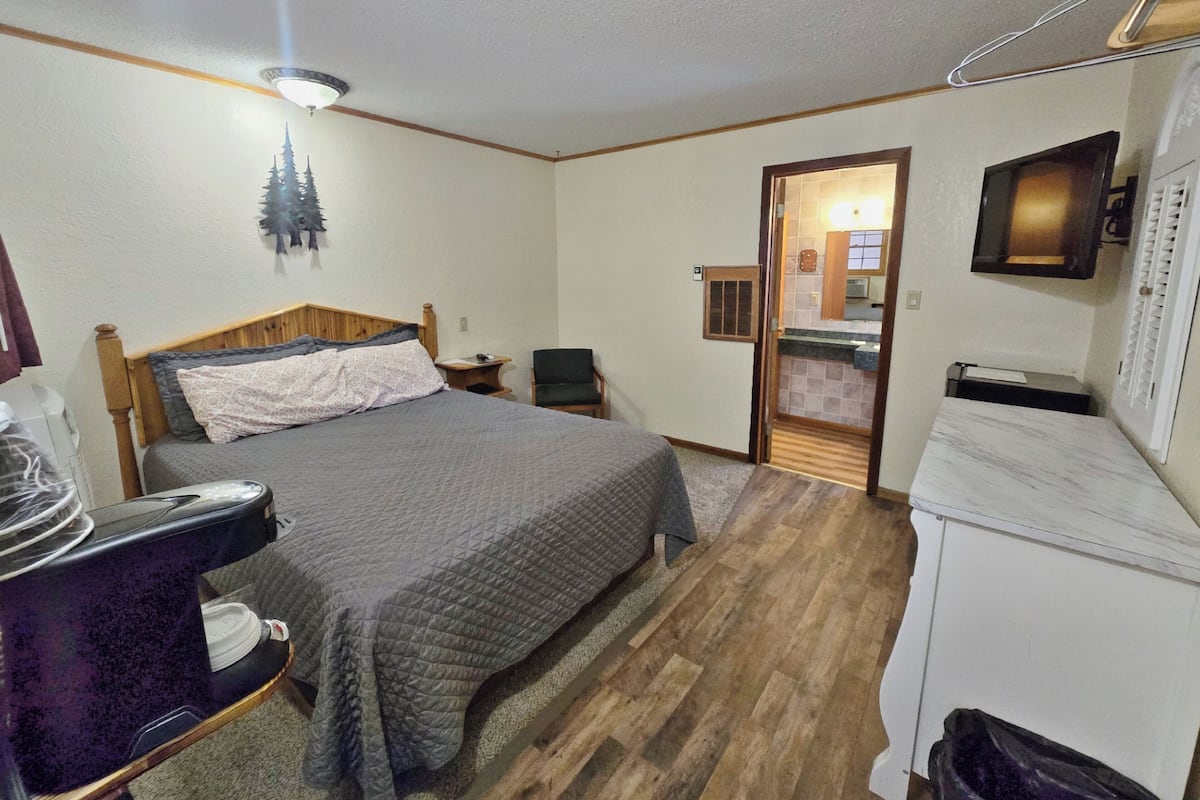 A bedroom with a bed, a chair, a small table, a microwave, and a cabinet.