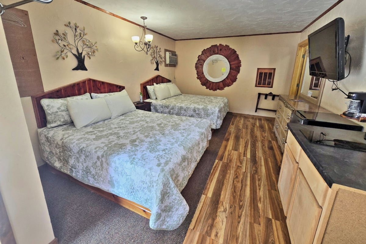 A hotel room with two beds, a wooden floor, a TV, and a coffee machine.