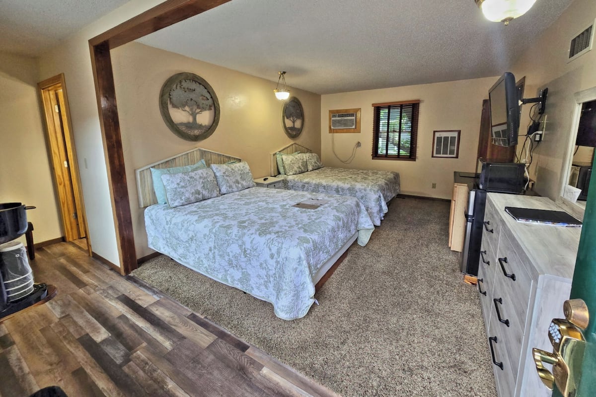 A bedroom with two beds, a dresser, a desk, and a window.