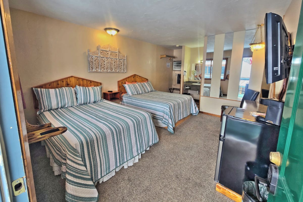 A room with two beds, a mirror, a television, and a sink.