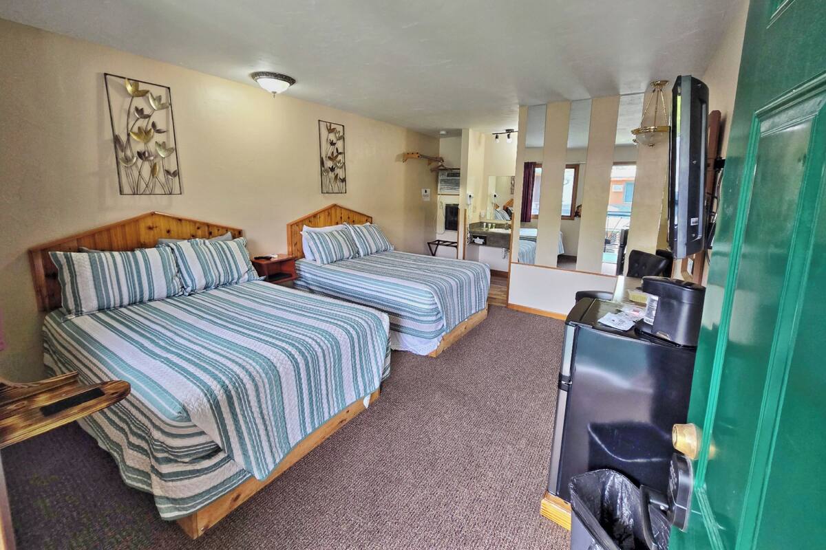 A room with two beds, a desk, a mirror, and a green door.