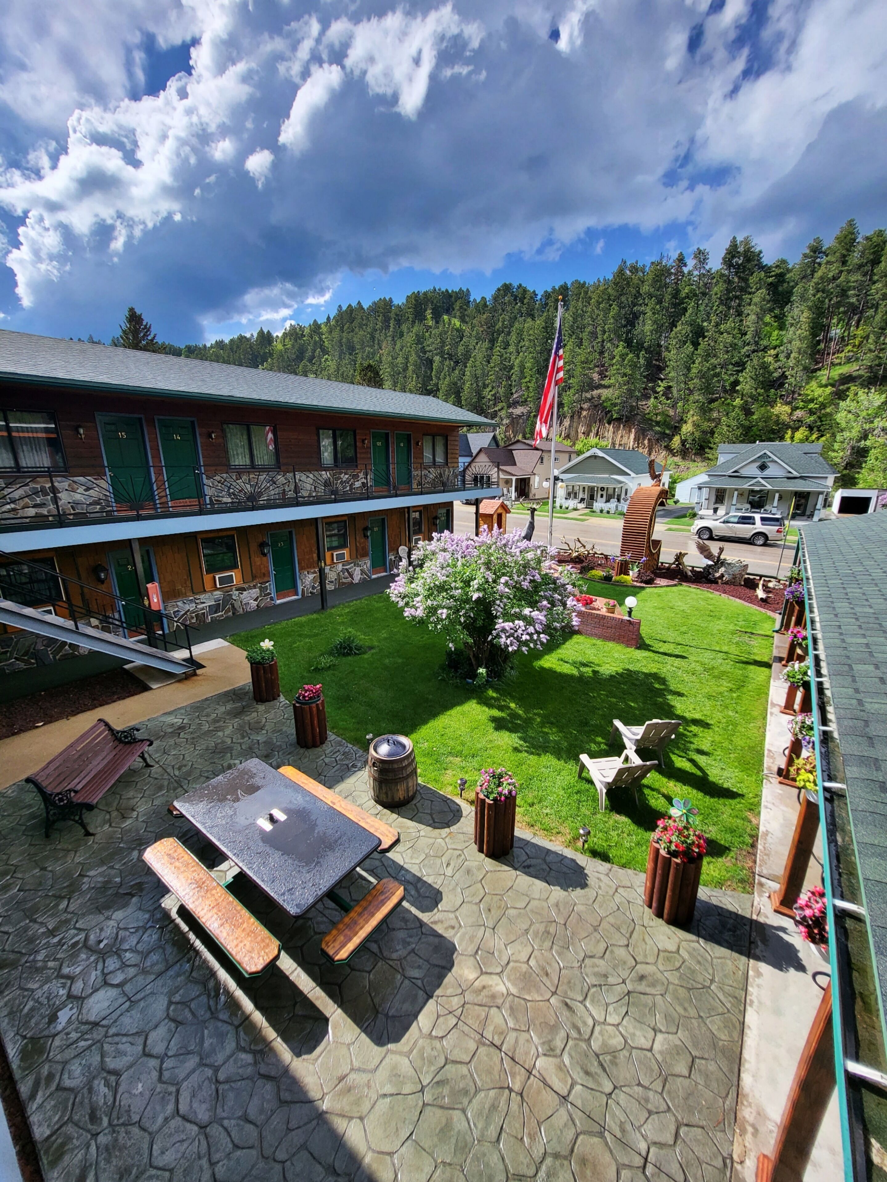 Eine Lodge mit einer Steinterrasse, Sitzgelegenheiten im Freien und Blick auf einen bewaldeten Hang.
