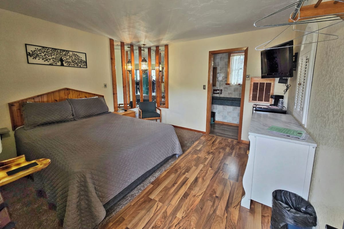 A bedroom with a wooden bed, a chair, a desk, and a television.