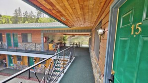 A wooden interior with a green door marked '15', a balcony with a metal railing, and a view of a building with green shutters. - Cedar Wood Inn (Deadwood)