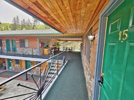 Interior de madera con una puerta verde marcada '15', un balcón con barandilla de metal y vistas a un edificio con contraventanas verdes.