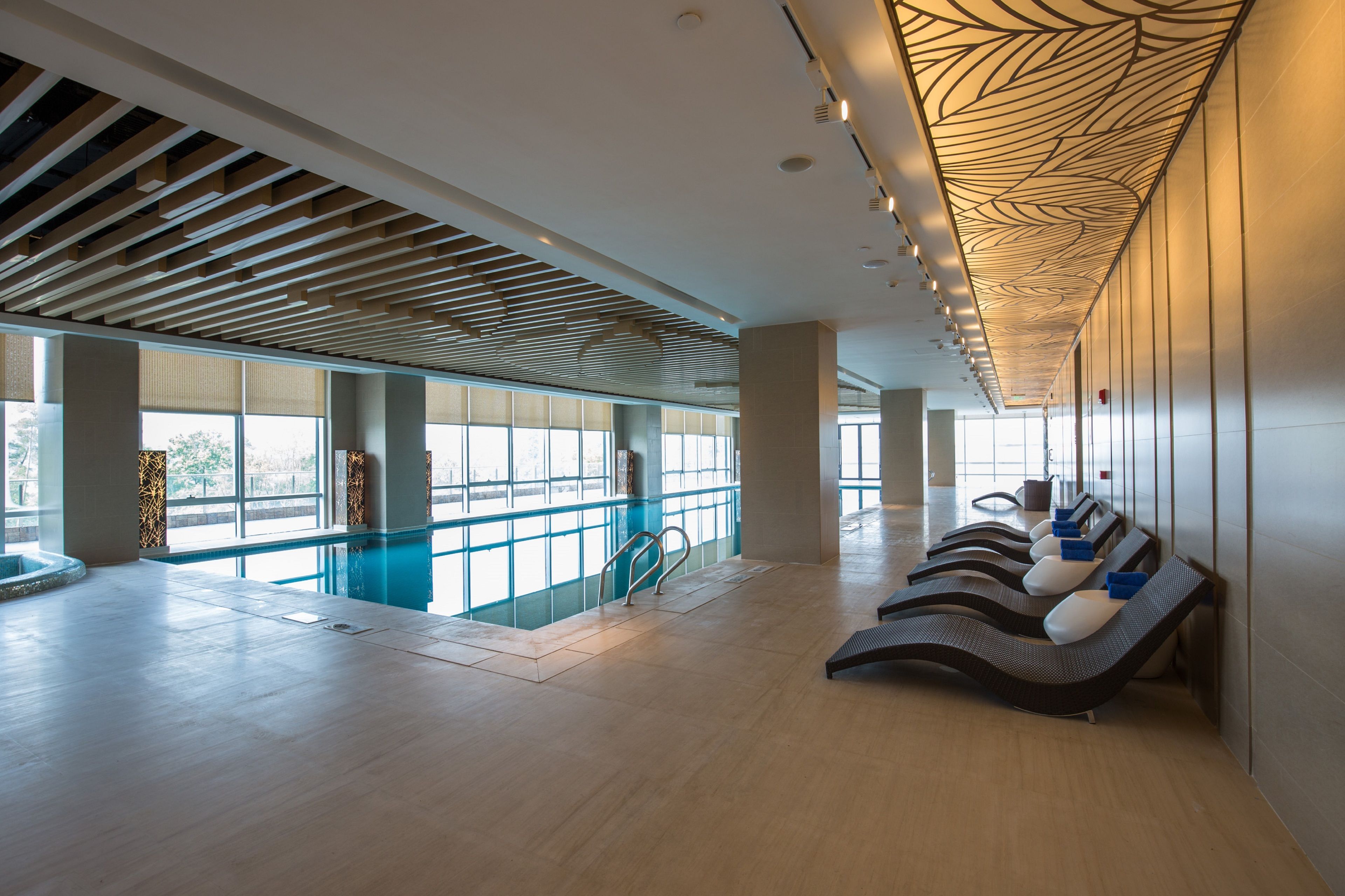 Amplio espacio interior con piscina, sillas de sol y ventanas grandes.