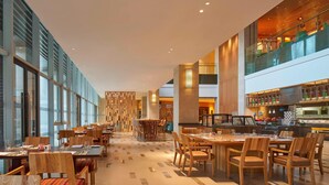 Un amplio vestíbulo de hotel con varias zonas de comedor, ventanas grandes y una decoración interior moderna.