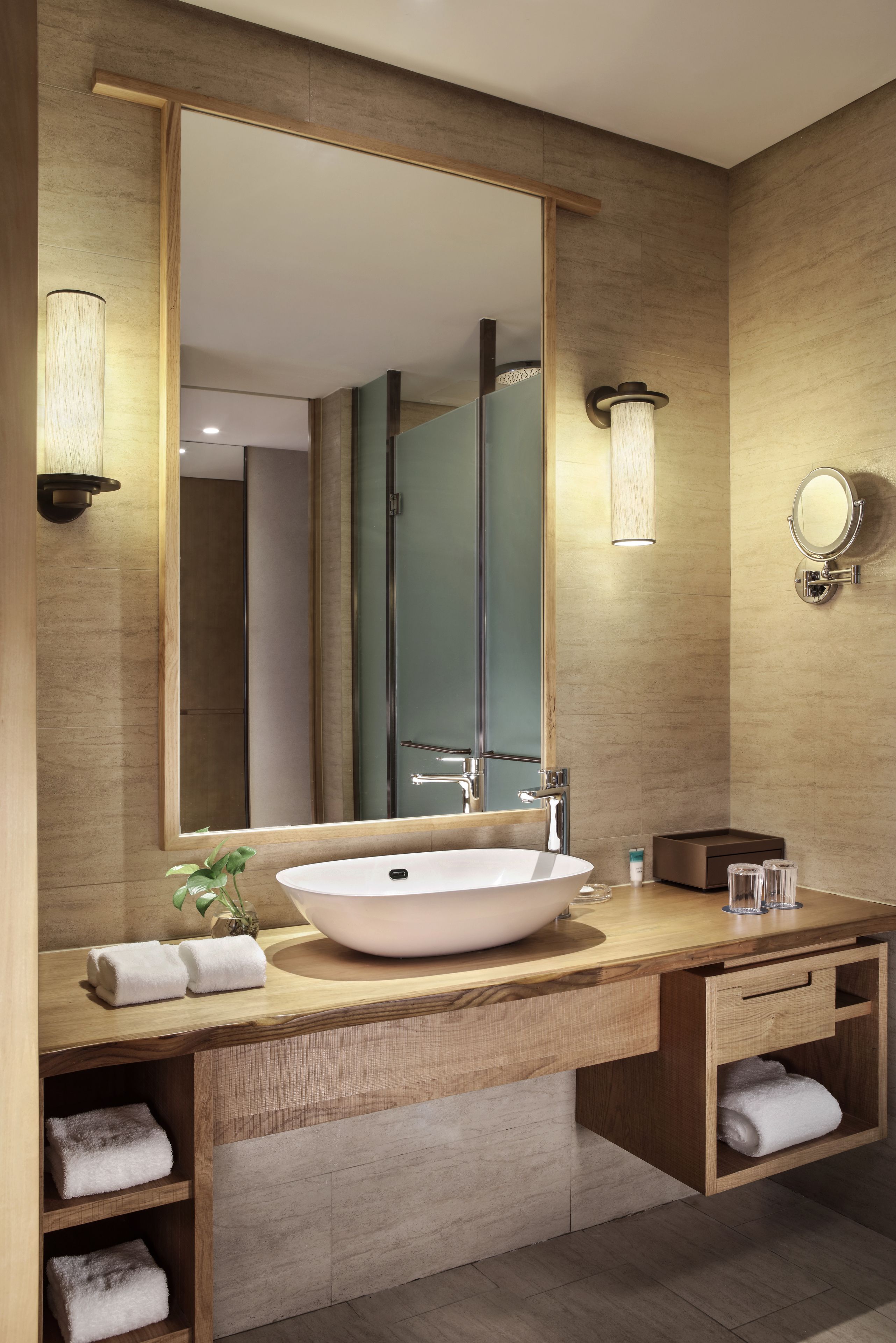 Un baño moderno con un espejo grande, un lavamanos de pedestal, tocador de madera y espacio para toallas integrado.