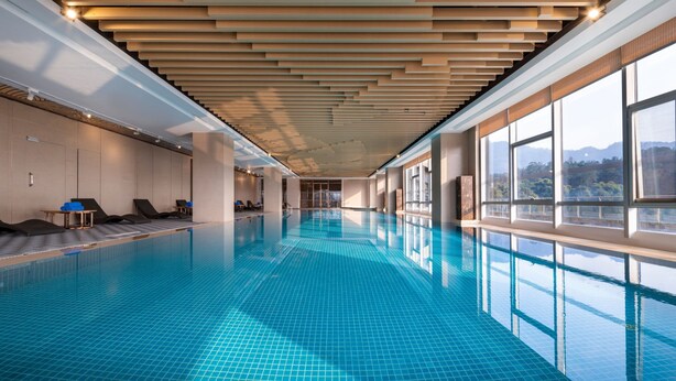 Una piscina interior larga con techo de madera y ventanas amplias.