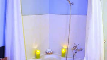 Una bañera grande independiente con cabezal de ducha, dos velas encendidas y una cesta con toallas dobladas.