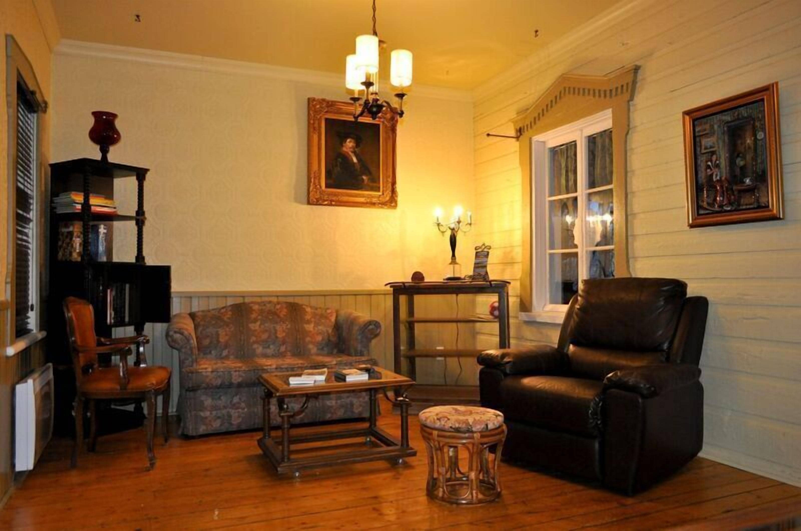 A cozy living room with a wooden floor, a patterned sofa, a leather armchair, a coffee table, and a bookshelf.