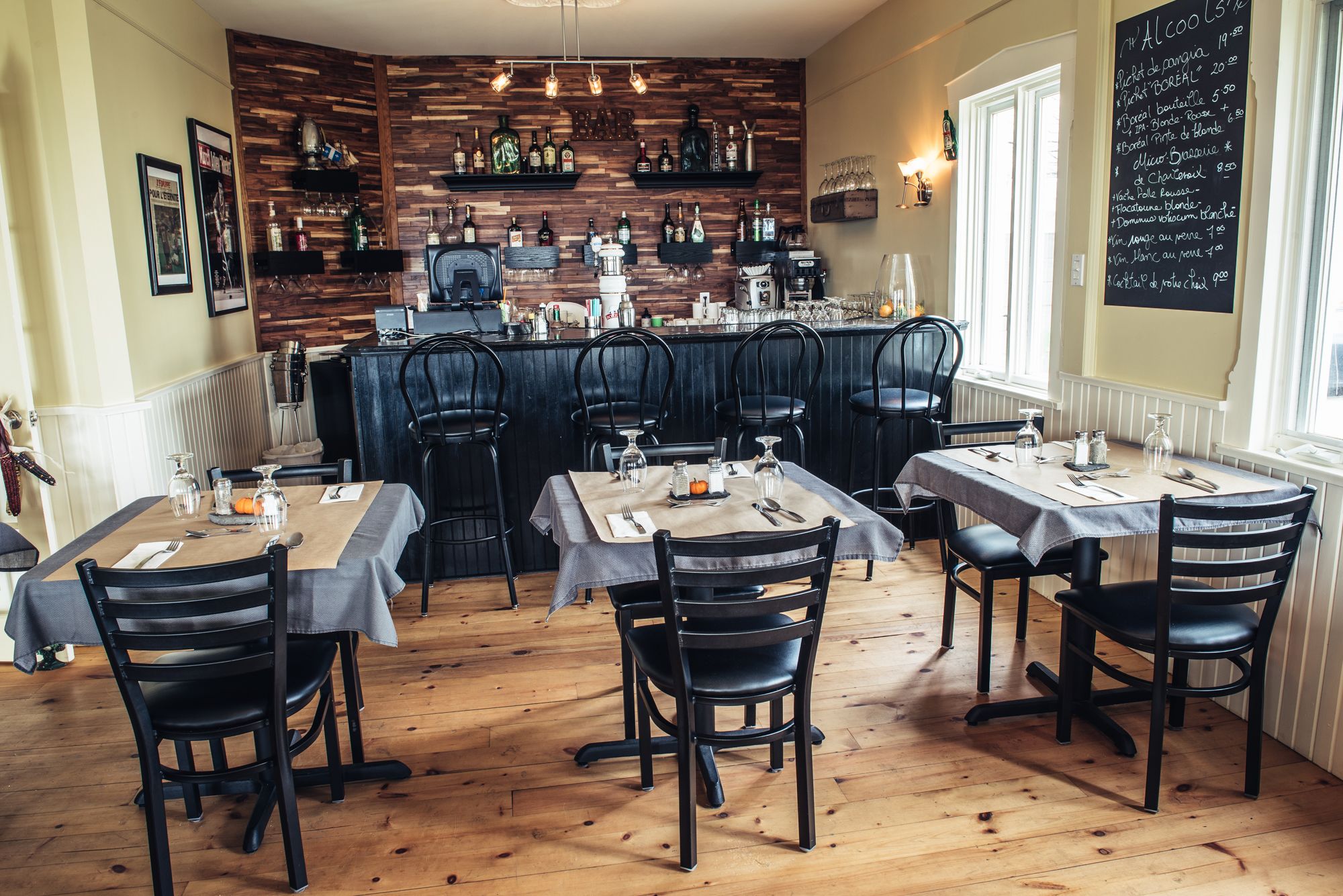 Un restaurant aux murs en bois, avec un coin bar et des tables dressées pour le service.