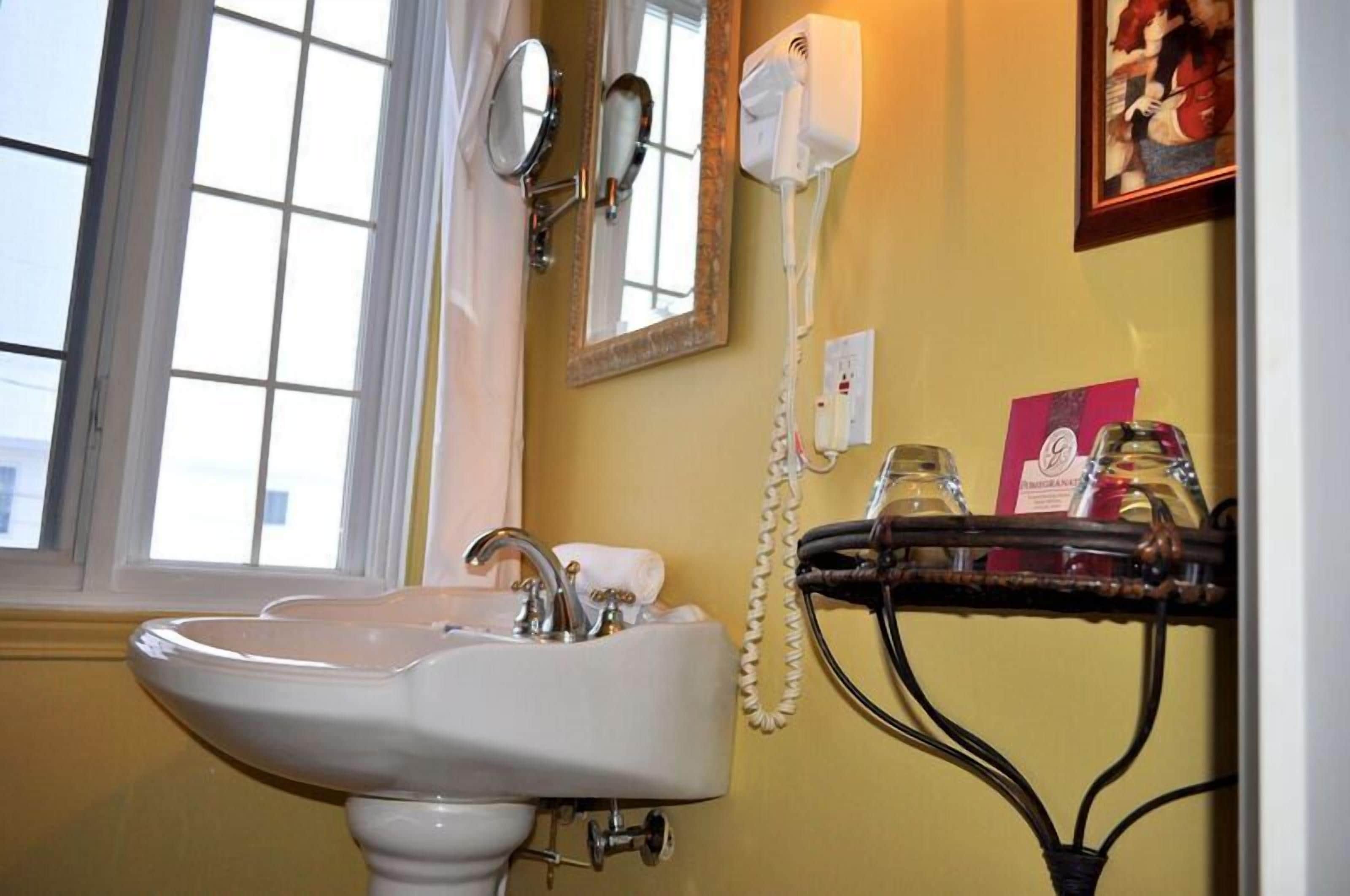 A bathroom with a white sink, a mirror, a hairdryer, and a window.