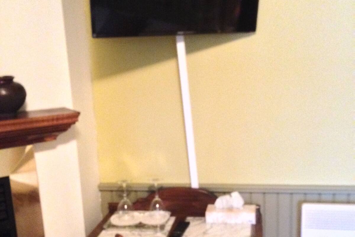 Ein Essbereich mit einem Tisch für zwei Personen, einem an der Wand montierten Fernseher und einem Holzstuhl mit gemustertem Sitzkissen.