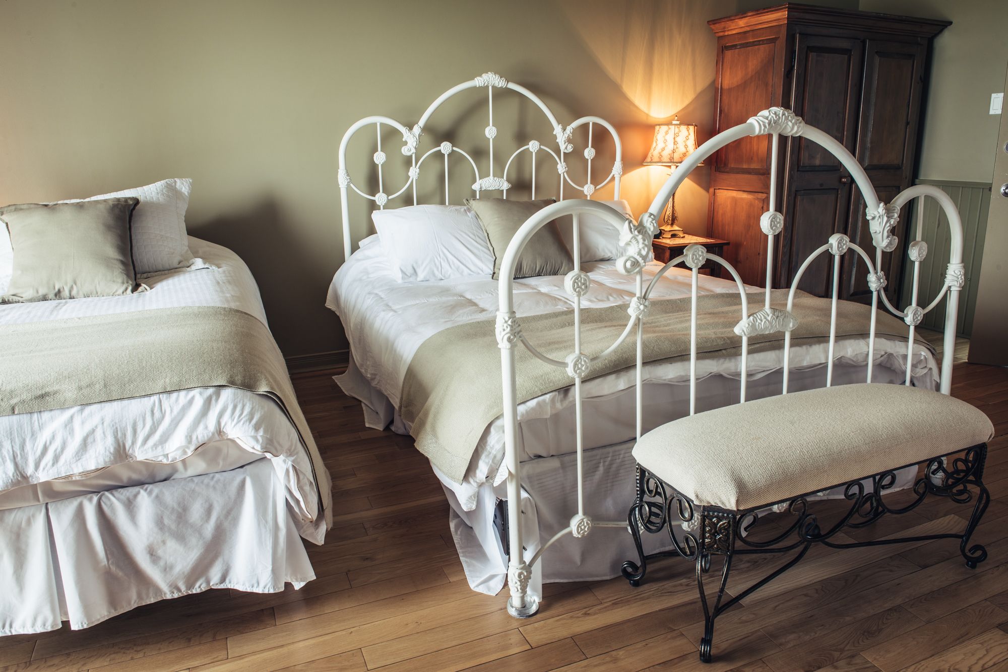 Une chambre avec deux lits, un banc et une table de chevet avec une lampe.