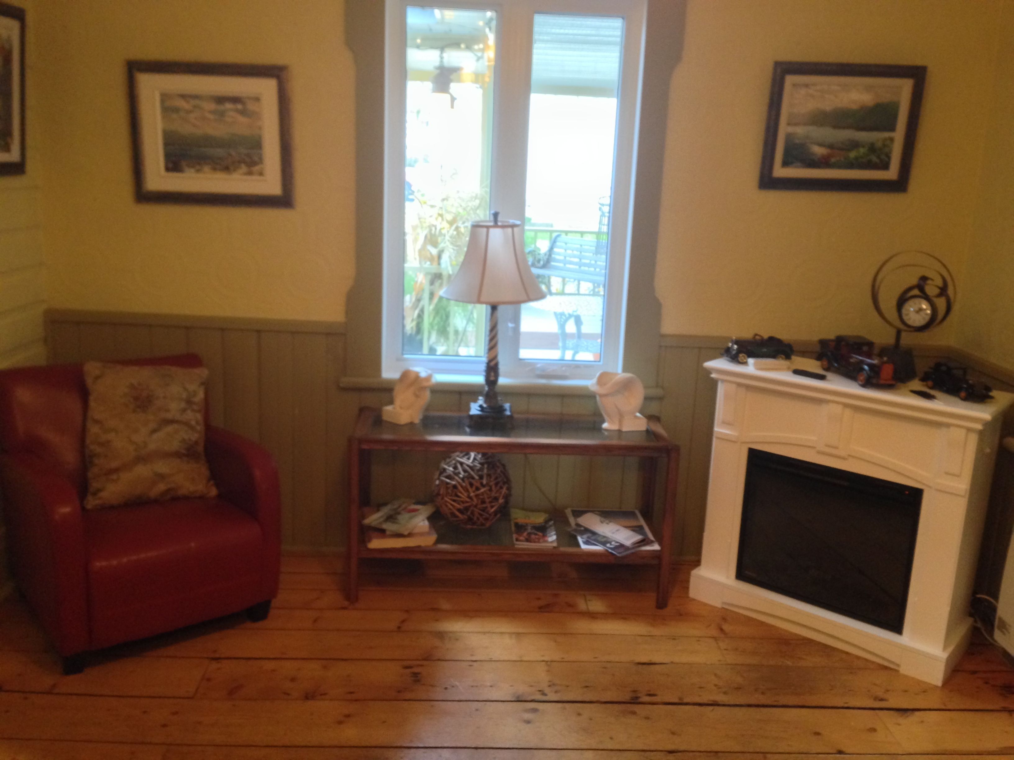 A living room with a red armchair, a wooden coffee table with decorative items, a fireplace, and two framed pictures on the walls.