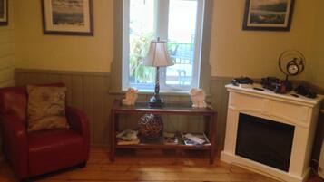 A living room with a red armchair, a wooden coffee table with decorative items, a fireplace, and two framed pictures on the walls.