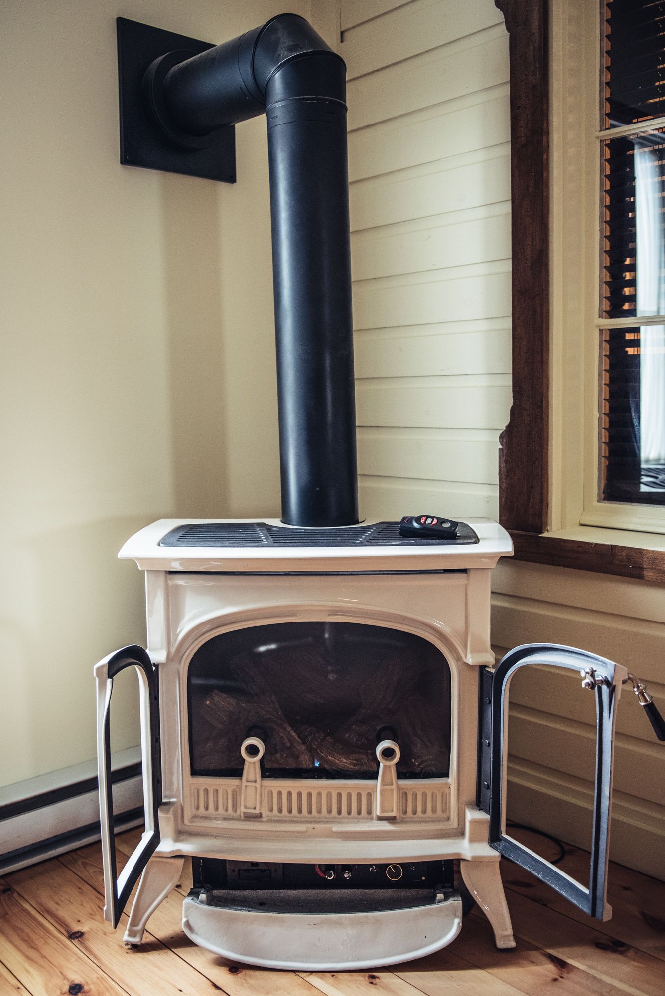 A wood-burning stove with a chimney, positioned against a wall with horizontal siding.