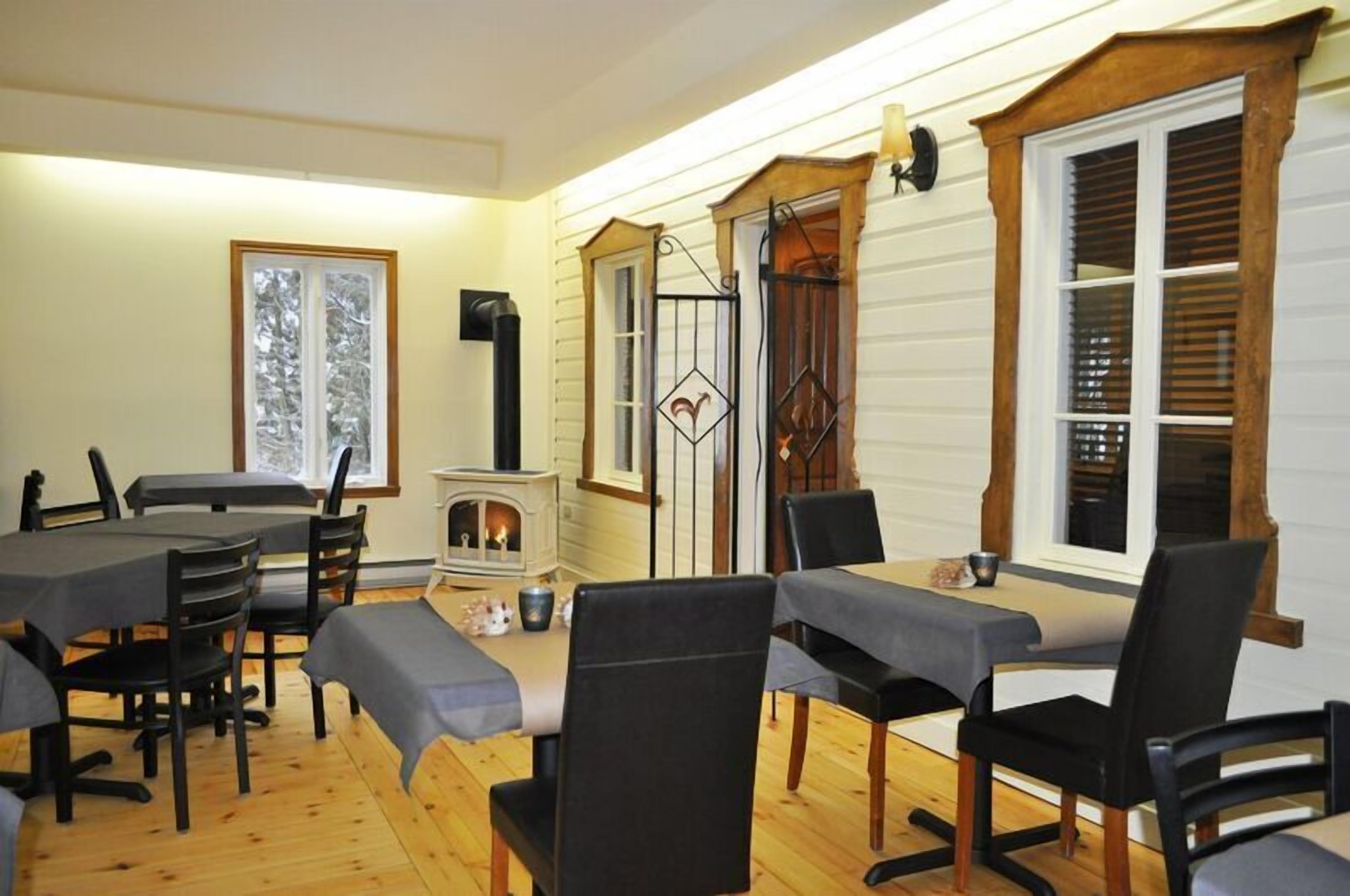 Un coin repas avec une table et des chaises en bois, une cheminée et une fenêtre équipée de stores.