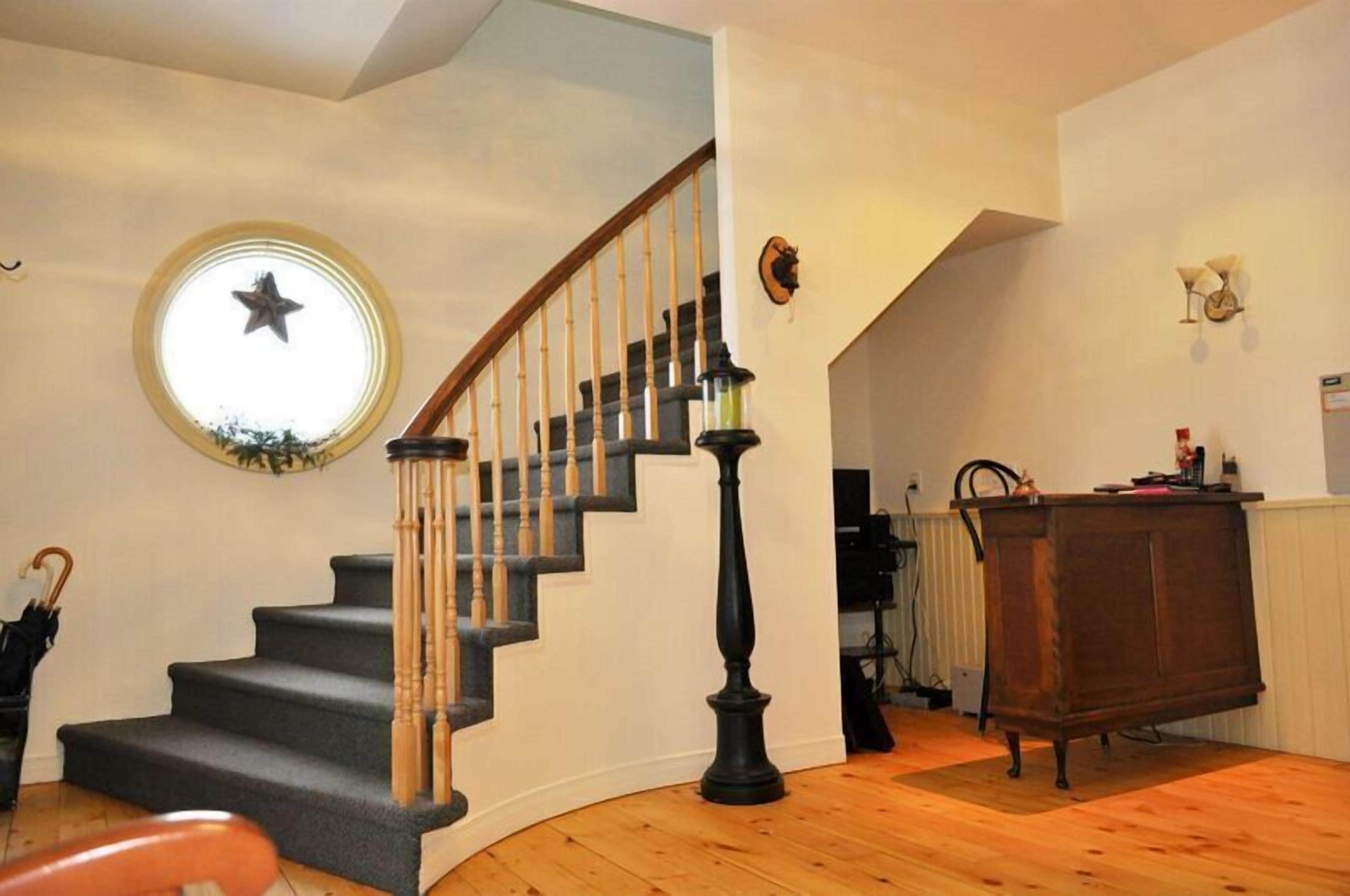 Un escalier avec des balustrades en bois et une main courante noire, un miroir rond orné d’une étoile et un meuble en bois dans une pièce dont le sol est également en bois.