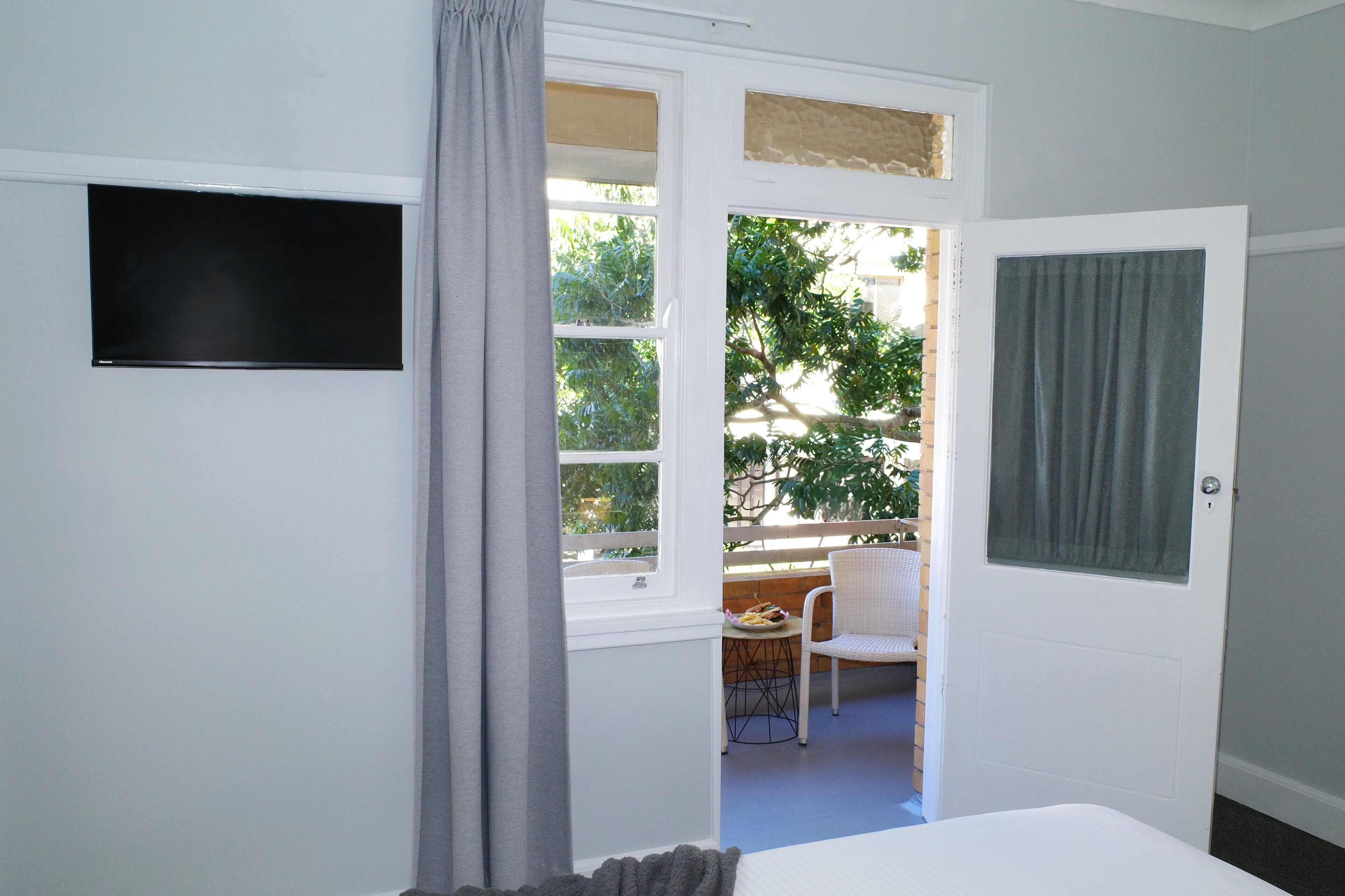 A room with a bed, a television mounted on the wall, and a door leading to an outdoor area with a table and chairs.