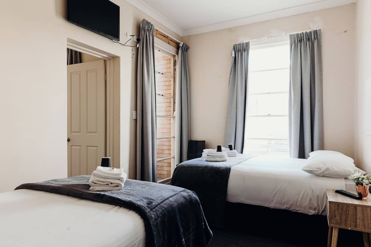 Quarto de hotel com duas camas, uma televisão presa à parede e uma janela com cortinas.