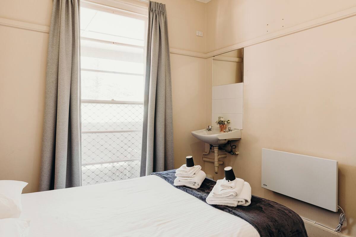 Quarto de hotel com cama, banheiro com pia e janela com cortinas.