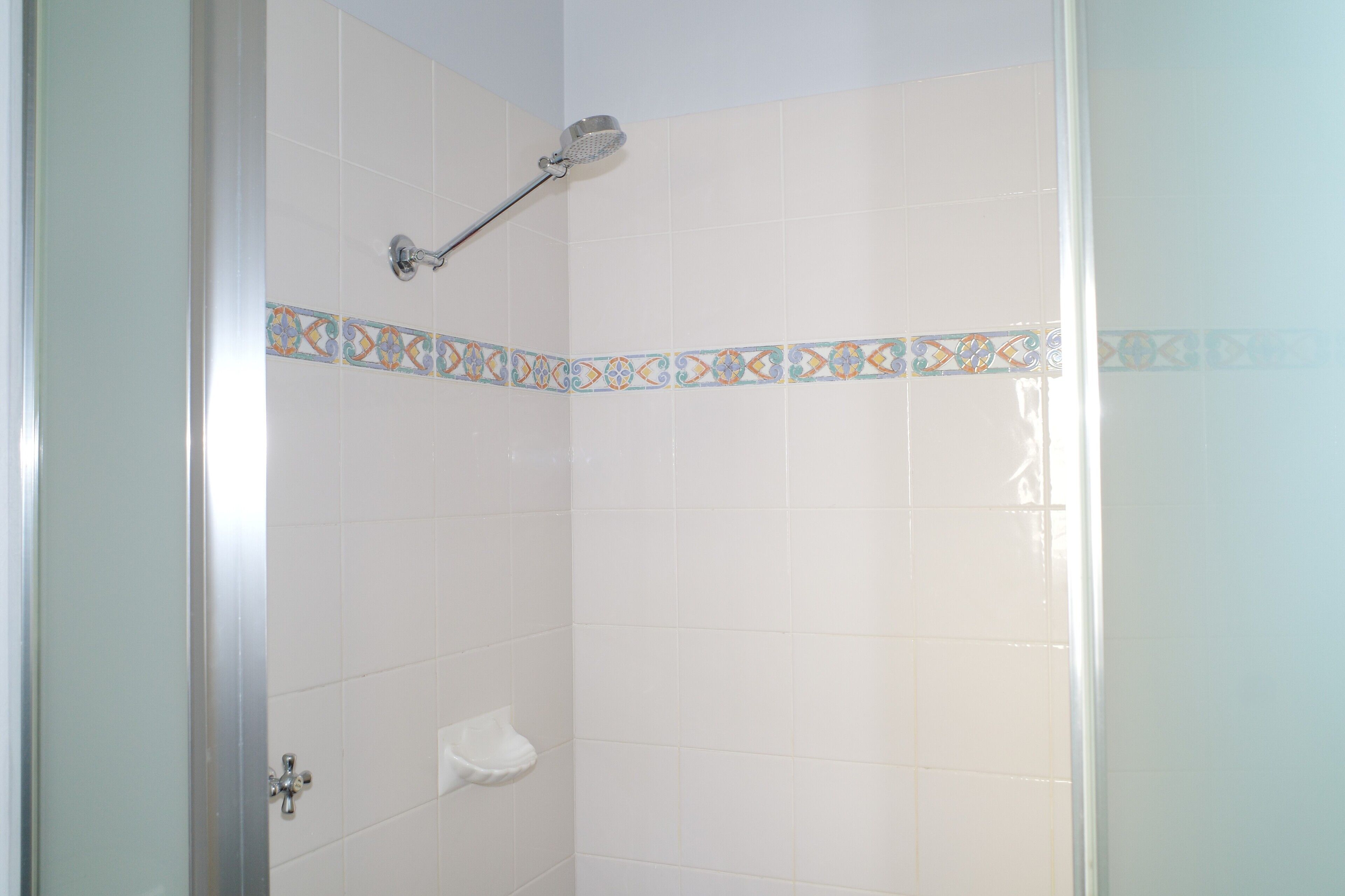 A shower with white tiles and a decorative border.