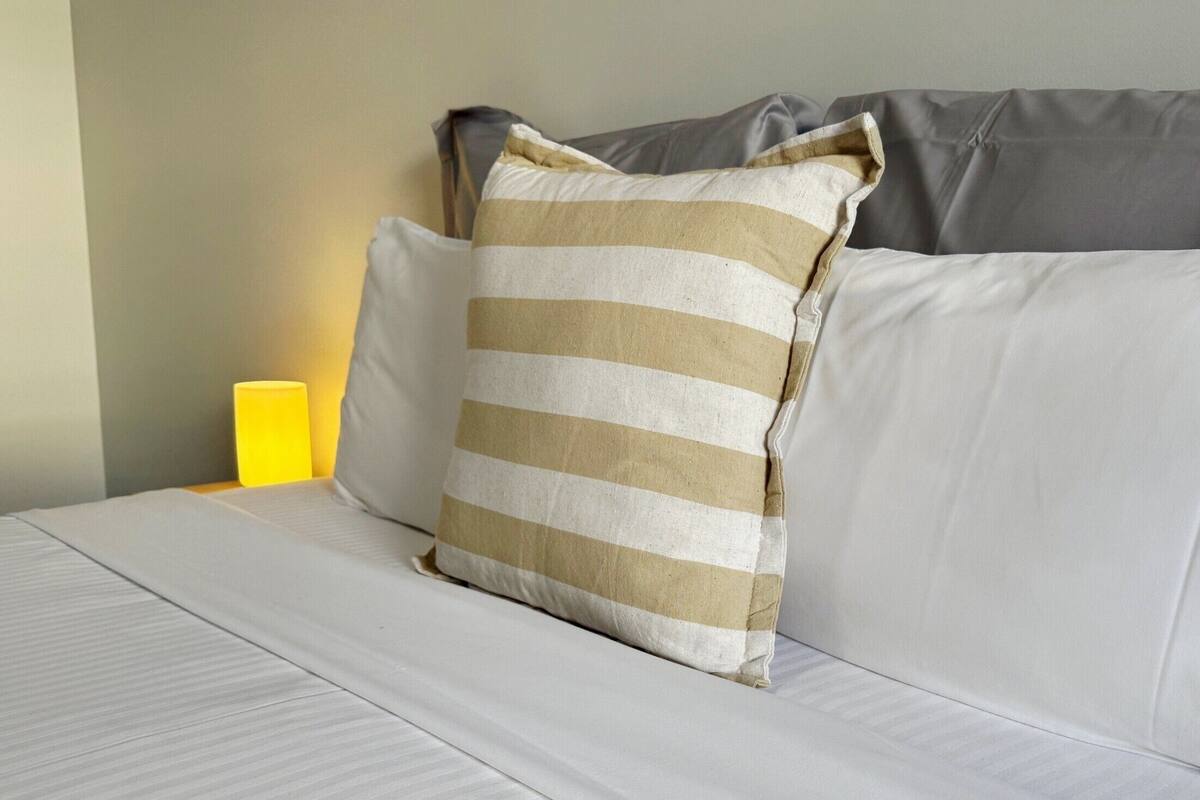 Cama bem arrumada com roupa de cama branca e almofada listrada.