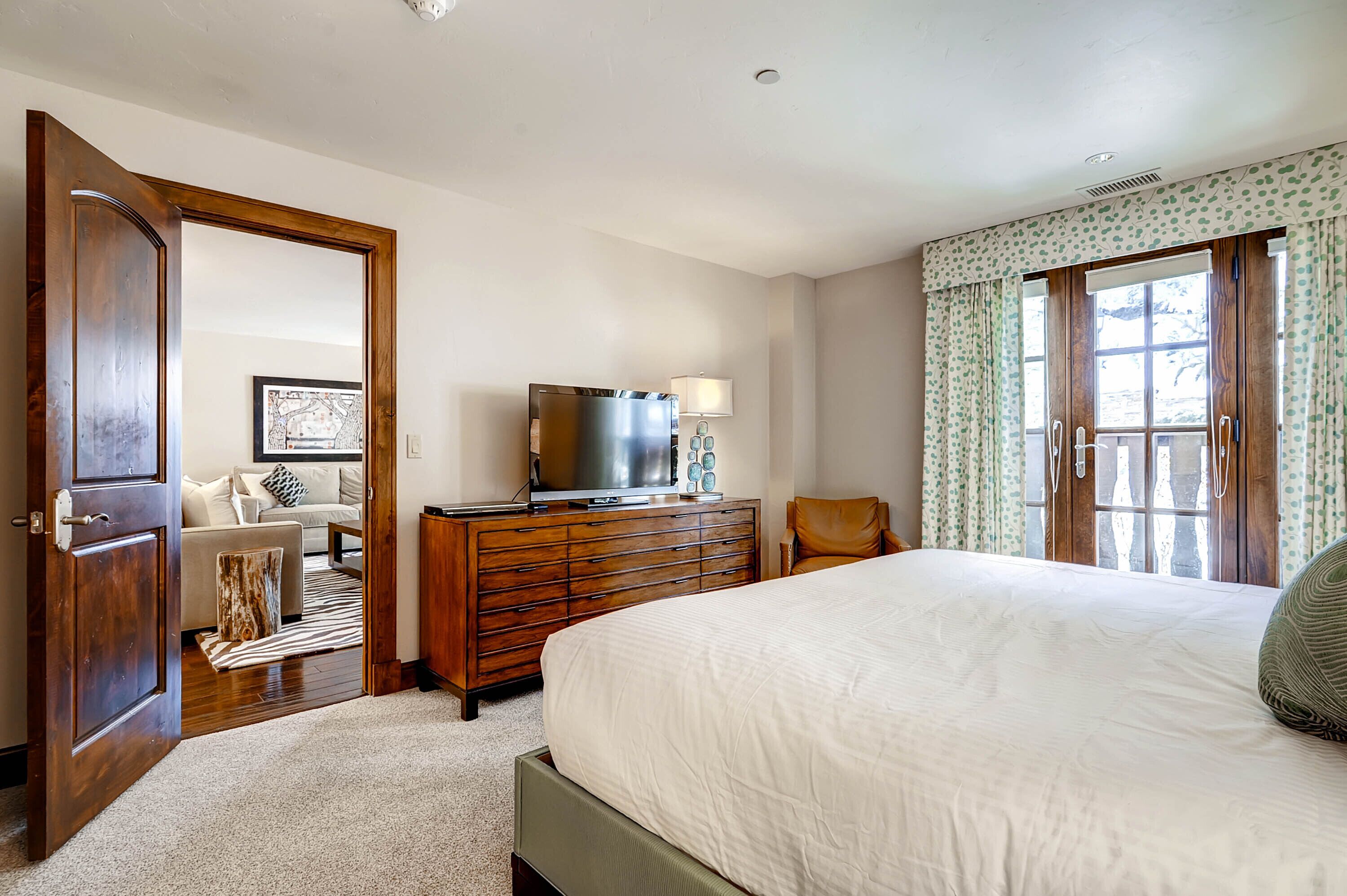 Une chambre à coucher comprenant un lit, une commode, un téléviseur et une vue sur l’extérieur par une fenêtre.
