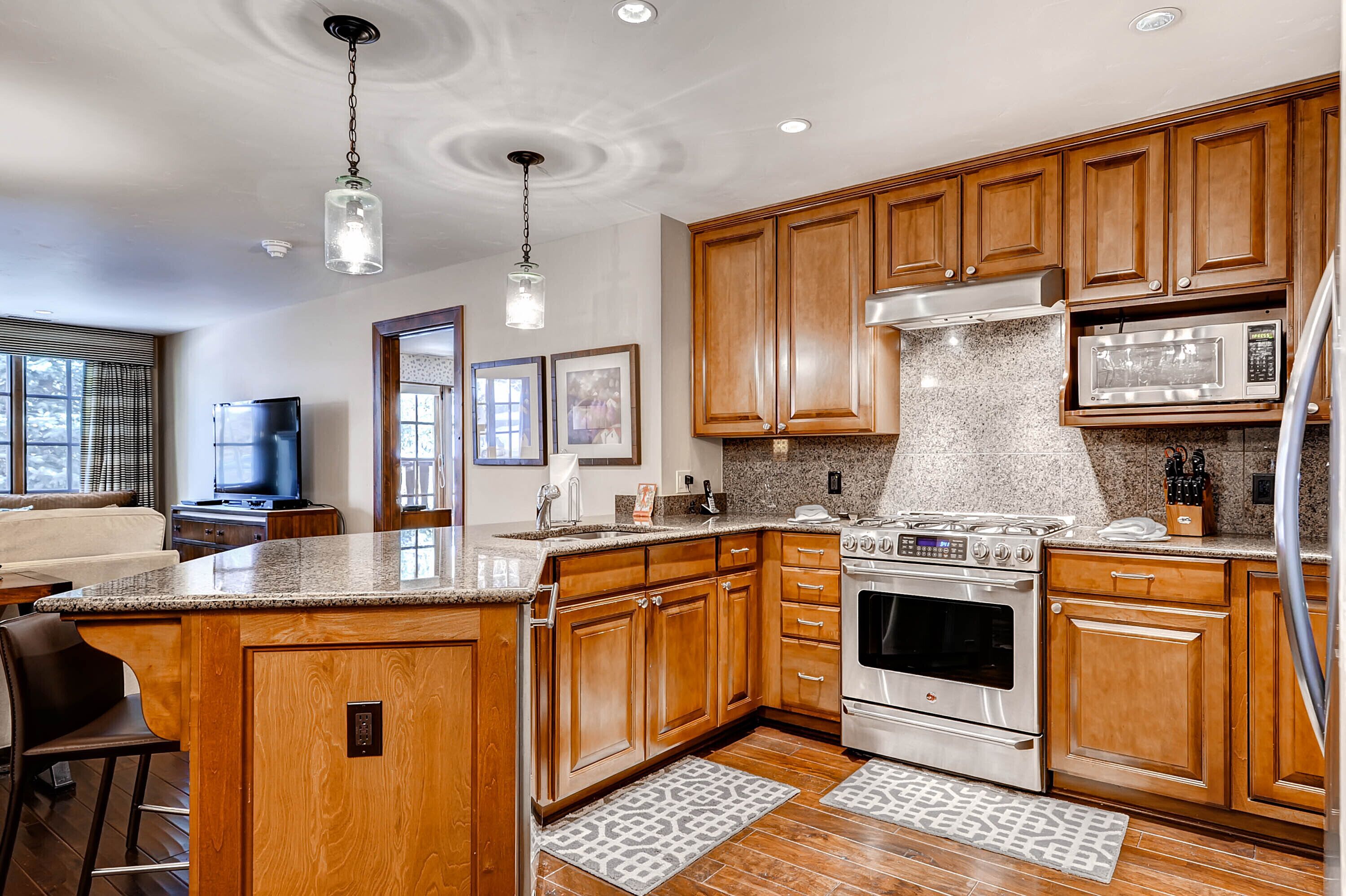A modern kitchen with wooden cabinets, granite countertops, stainless steel appliances, and pendant lighting.