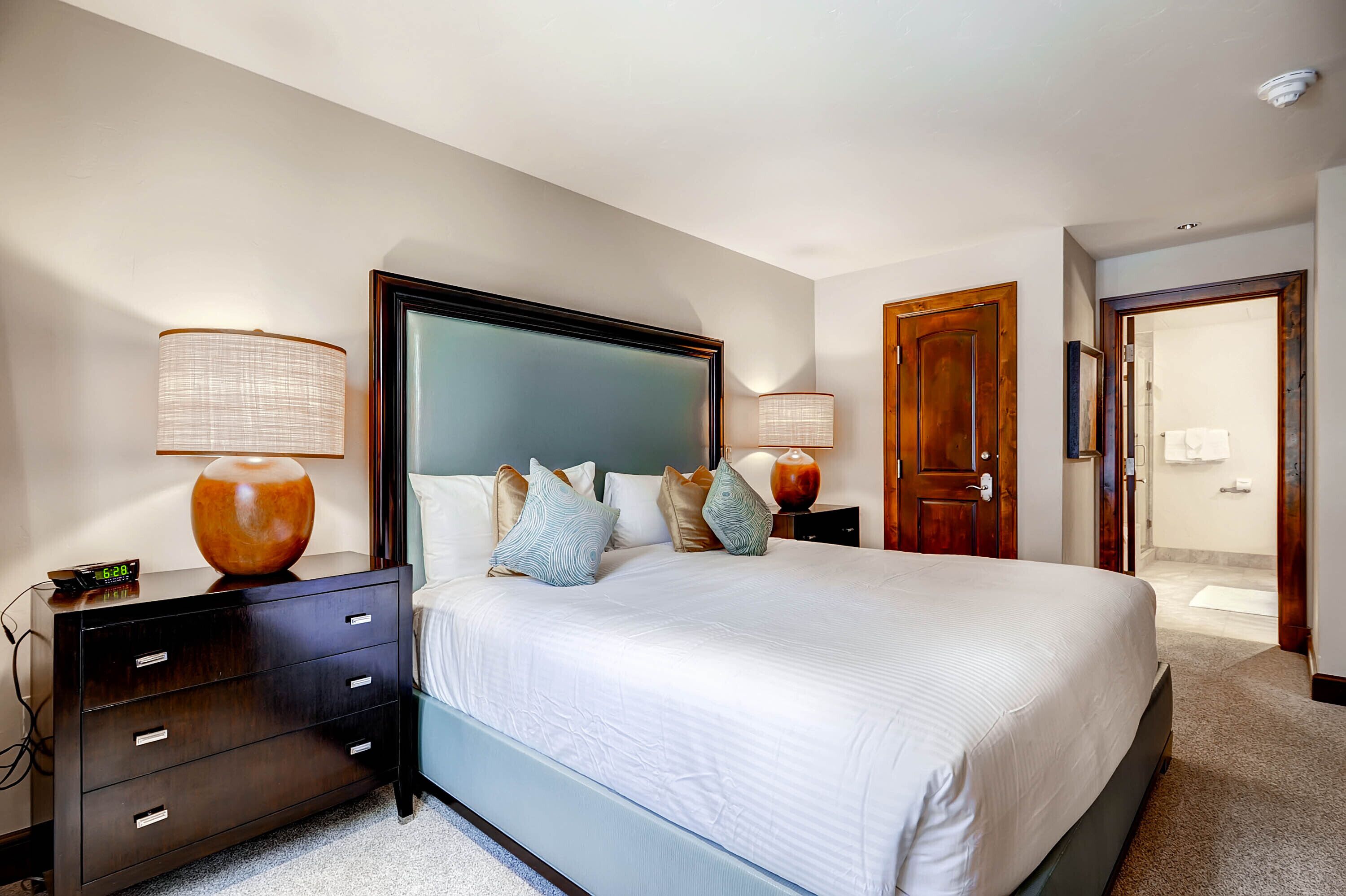 A neatly arranged bedroom with a large bed, bedside tables, and a wooden door.