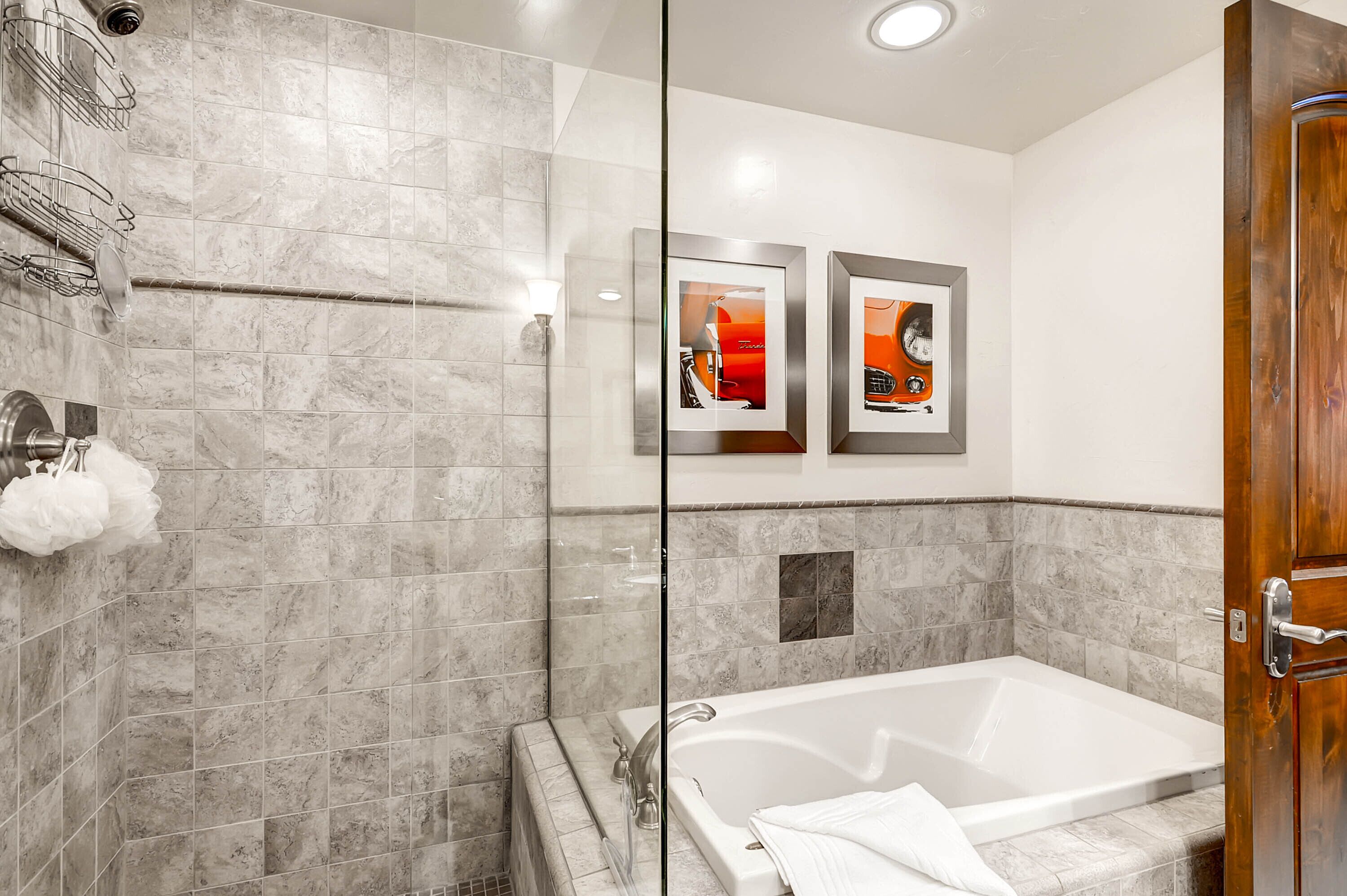 Een moderne badkamer met een douchecabine van glas, een witte badkuip en twee ingelijste foto’s aan de wand.